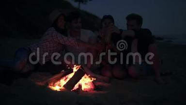 年轻人野餐，晚上在海滩上篝火，喝啤酒，做<strong>欢呼声</strong>。 快乐的朋友